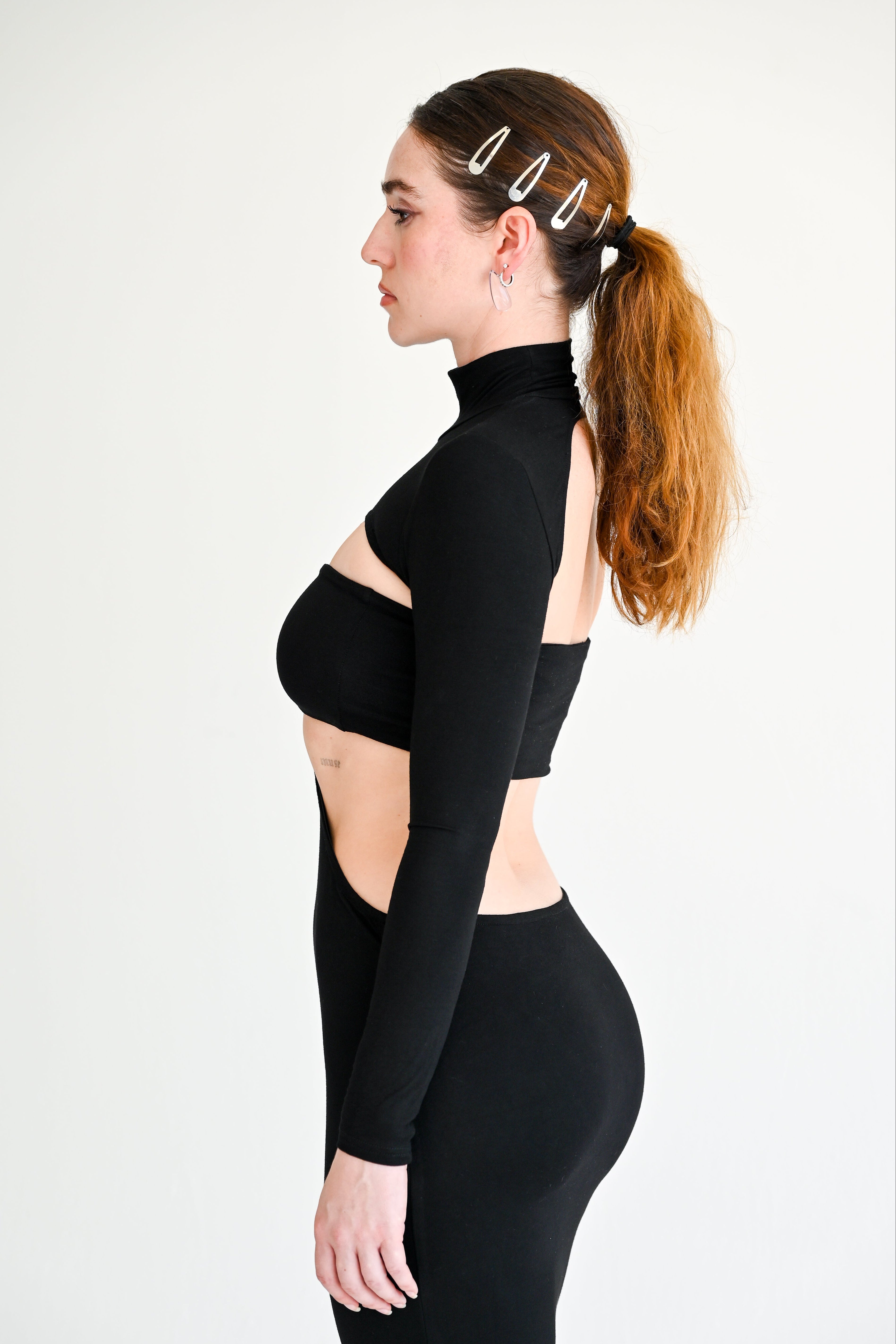 Woman wearing a black long-sleeve top with cut-out design and black leggings on a white background