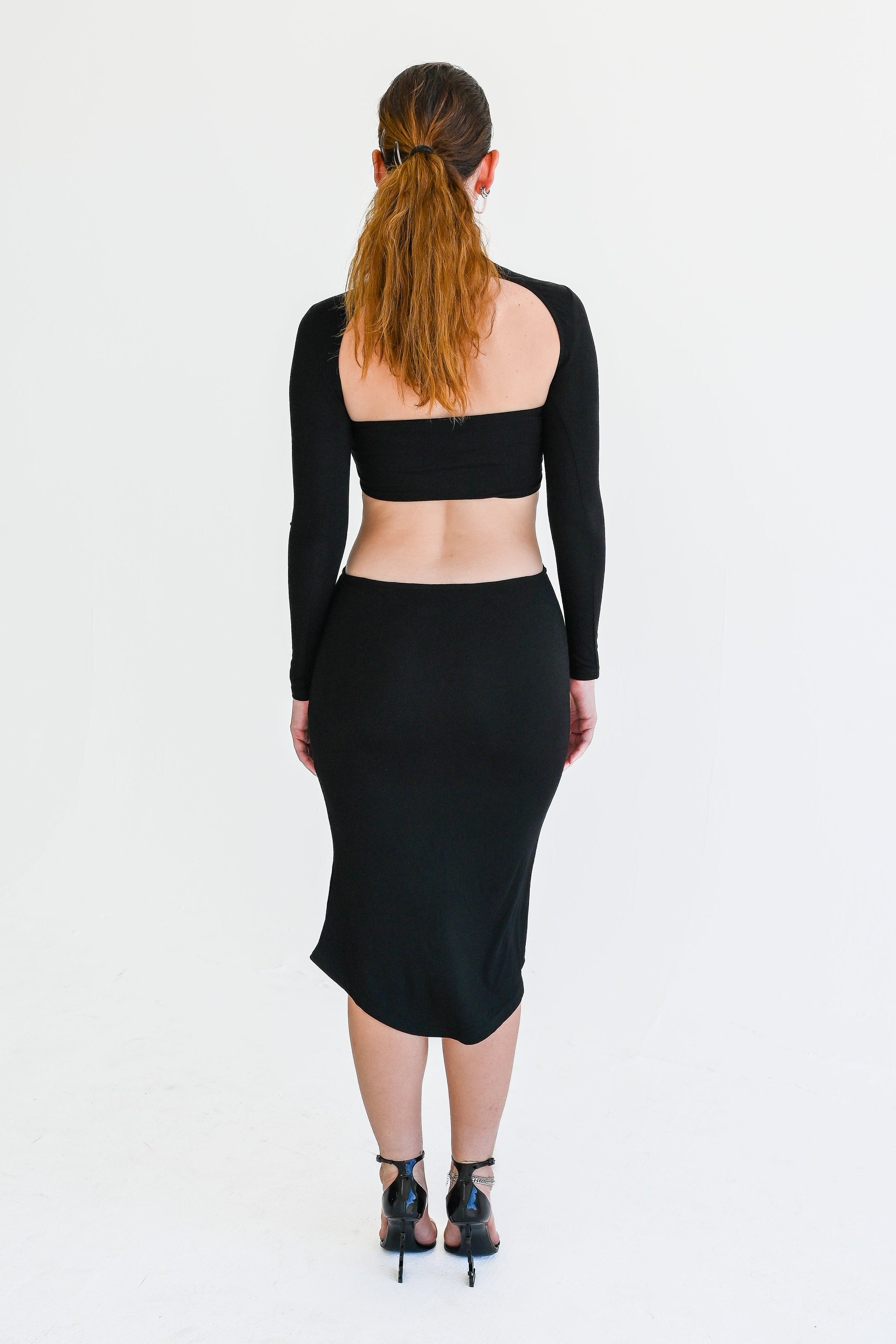 Person wearing a black long-sleeve crop top and skirt on a white background
