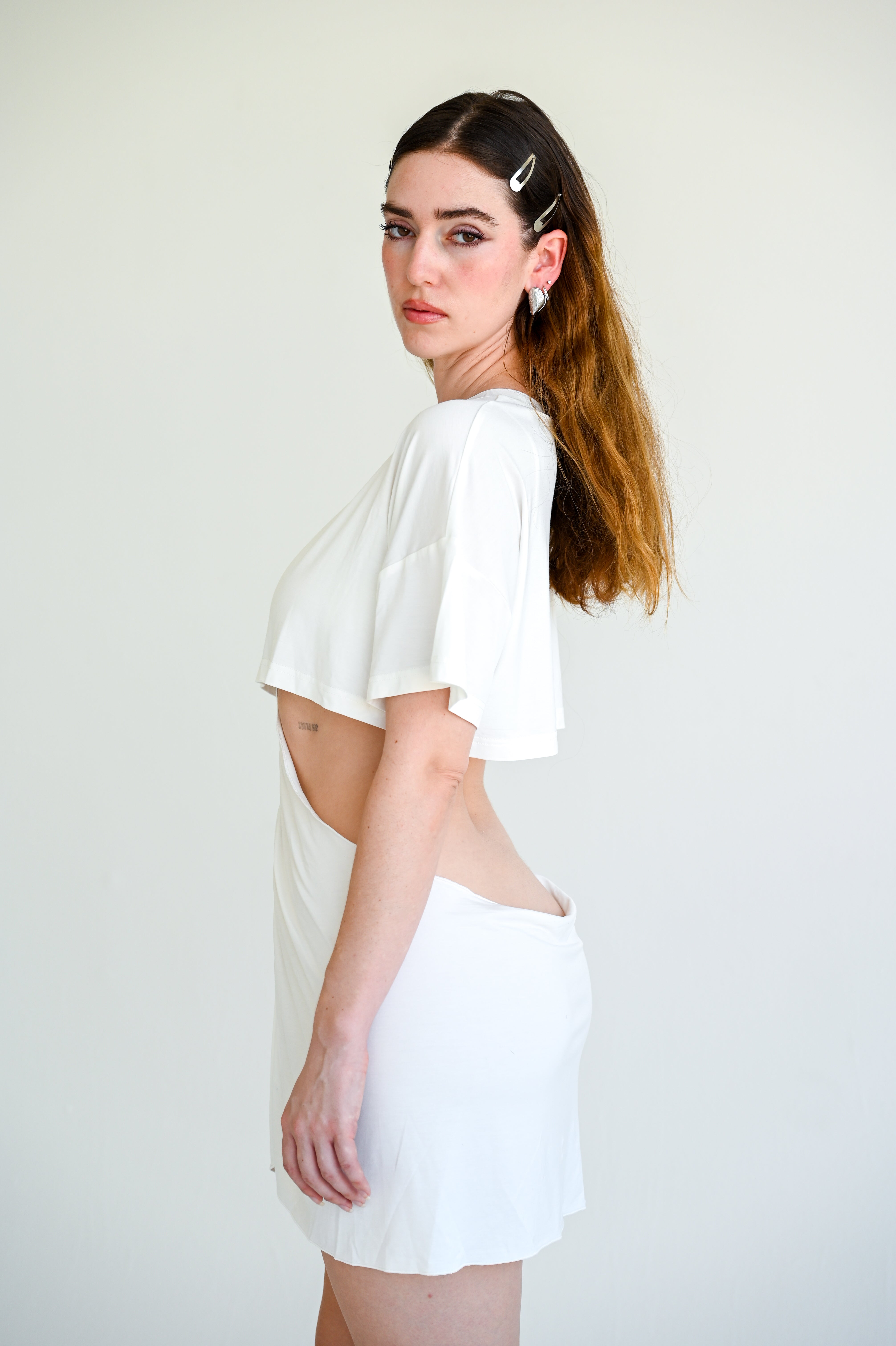 Woman wearing a white outfit with cut-out design on a plain background